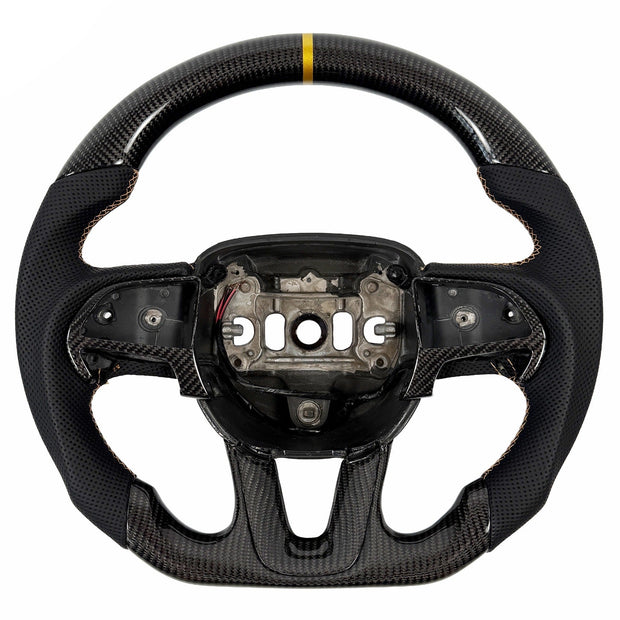 2015-2023 Dodge Charger and Challenger carbon fiber steering wheel by Texas Carbon, shown from the front with a gloss woven finish, black perforated leather grips, gold stitching, a gold 12 o'clock center stripe, matching carbon fiber button trim and lower-spoke trim, a round top and flat bottom, and an exposed airbag mounting hub.
