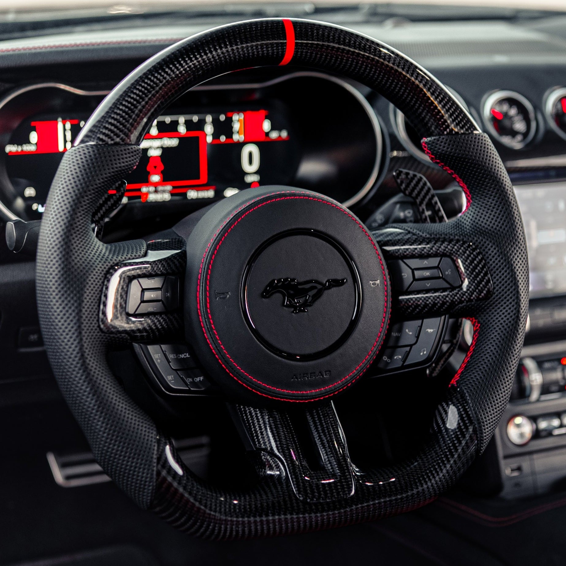2015-2023 Ford Mustang S550 carbon fiber steering wheel installed with red-stitched black perforated leather grips, flat-bottom design, and red center stripe