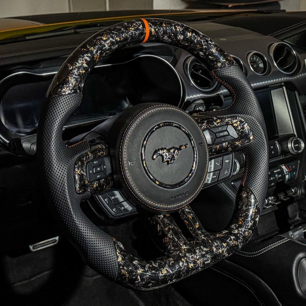 2015-2023 Ford Mustang S550 orange forged carbon fiber steering wheel installed with black perforated leather grips, flat-bottom design, and orange center stripe