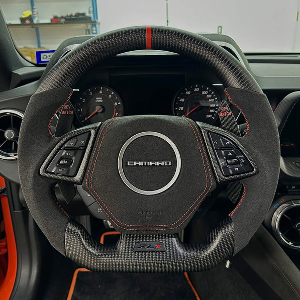 Carbon fiber and Alcantara flat-bottom steering wheel with orange stitching and an orange top-center stripe installed in a Chevrolet Camaro.