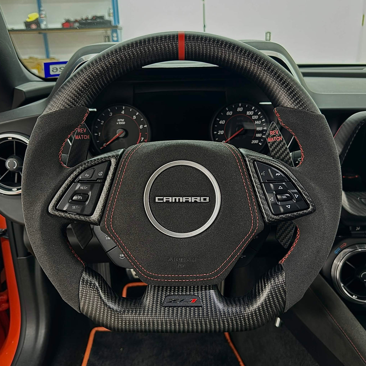 Carbon fiber and Alcantara flat-bottom steering wheel with orange stitching and an orange top-center stripe installed in a Chevrolet Camaro.
